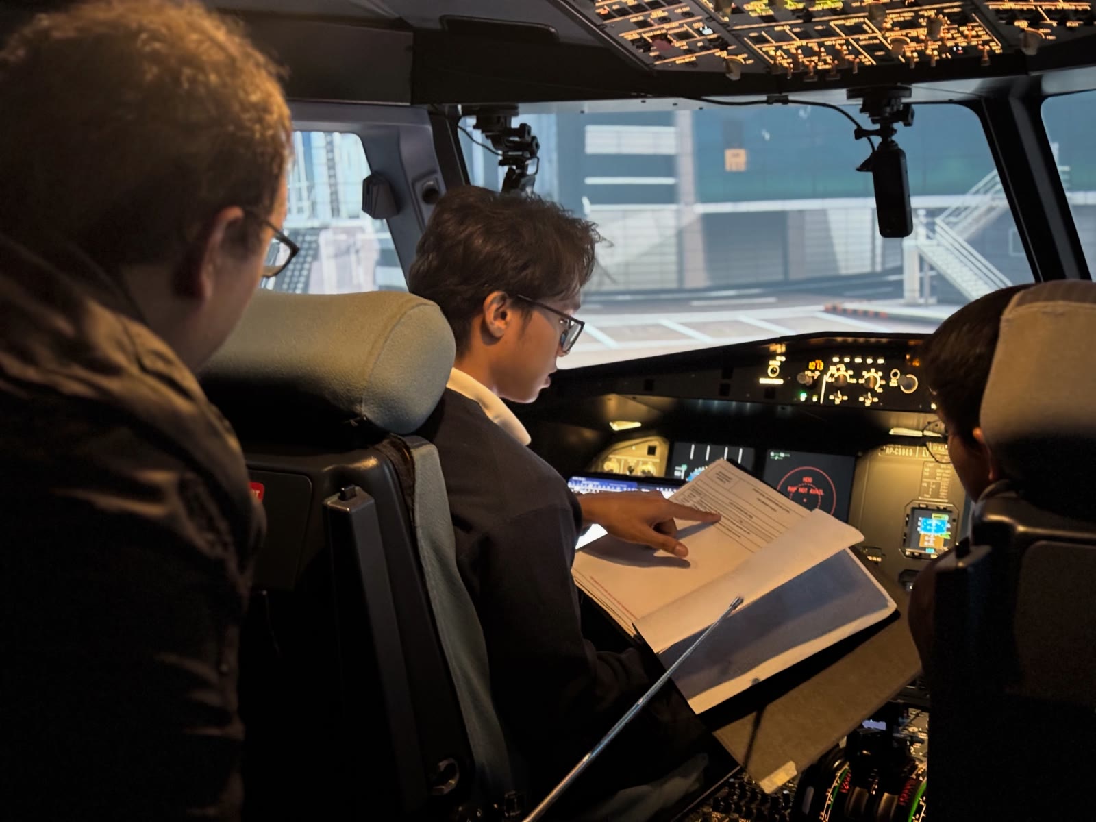 APOP Second Officer trainees reviewing a checklist together at the A320 flight deck controls during a night simulator session.