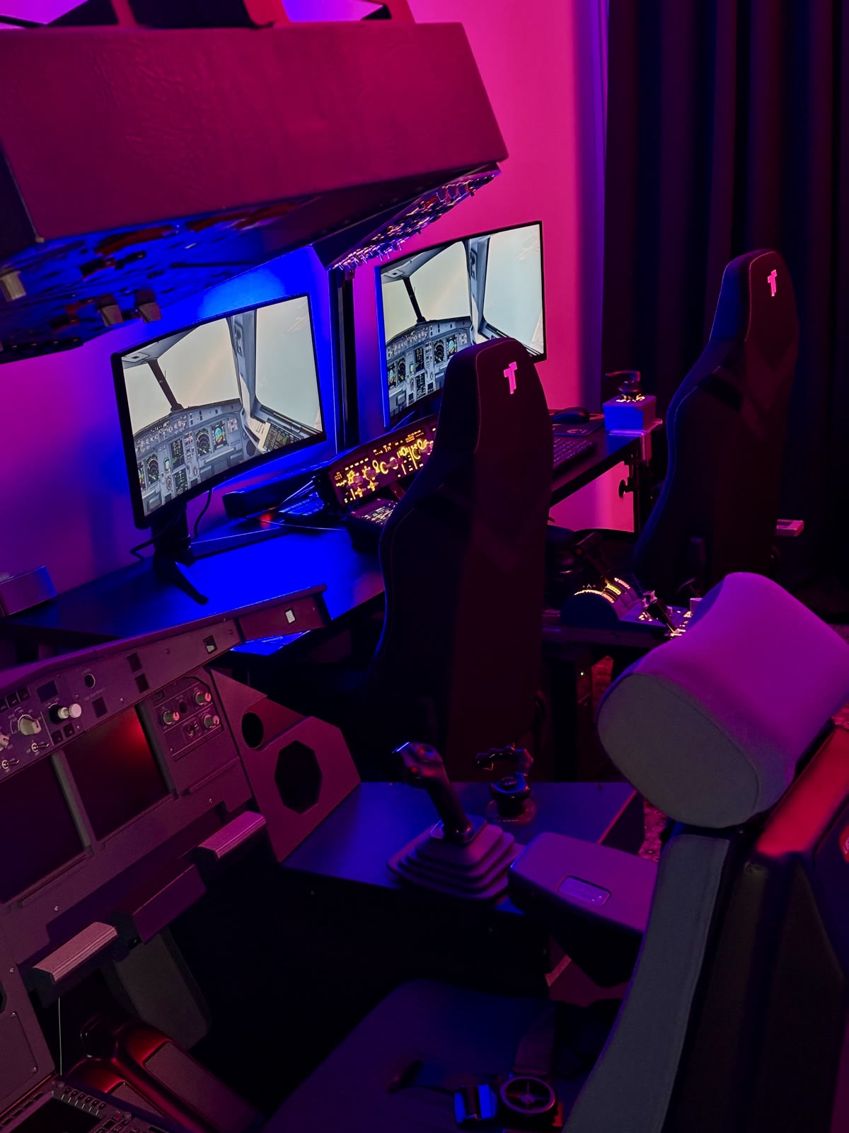 A pilot at the Aviation Simulator Station, dual displays showing the outside visual under moody cabin lighting.