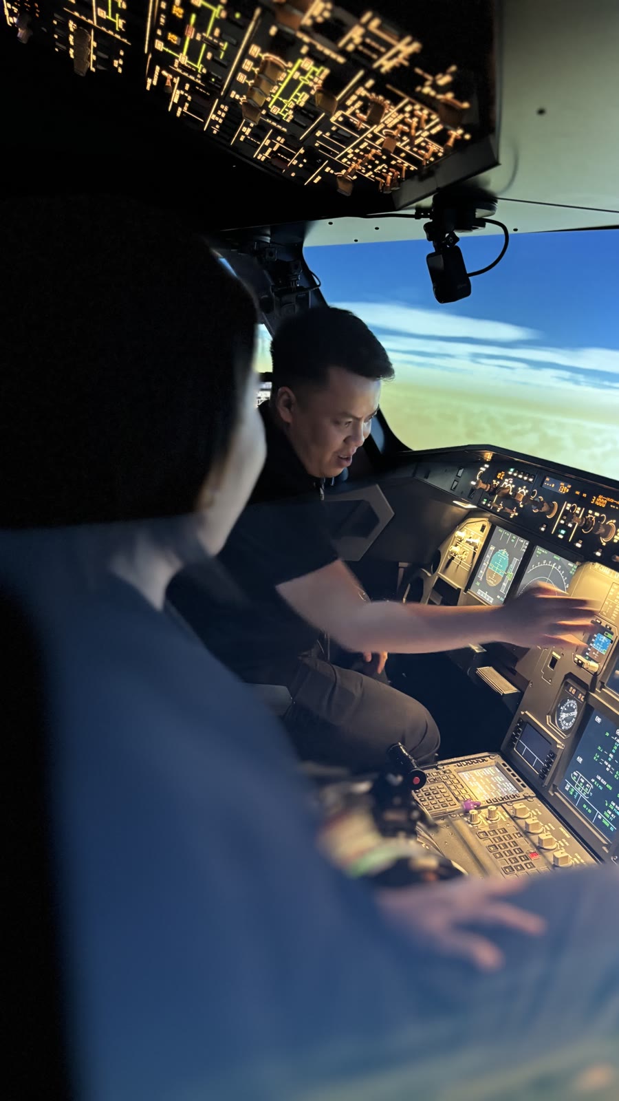 A flight coach guiding a trainee at the A320 simulator controls during a practice session at dusk.